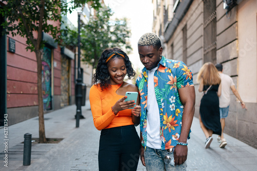 Young black friends looking at smartphone while walking
