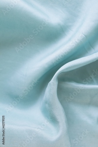 Light blue color natural silk draped in folds, top view, satin fabric texture, pastel shade