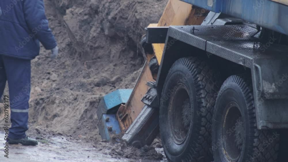 A worker in overalls watches the process of digging a hole with an excavator machine. Chassis and emphasis of the excavator, industry