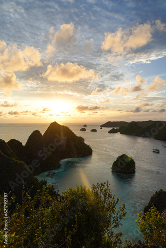 A view of the blue lagoon with a sunset sky, clear sea, some sailing ships and limestone islands in remote archipelago. View from the top of the Wayag Islands, Raja Ampat, West Papua, Indonesia.