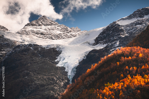 Snow-covered mountains and yellow autumn forest. Cheget mount in North Caucasus, Russia.