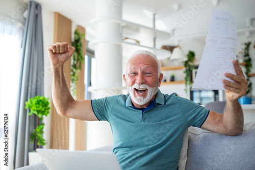 Surprised laughing happy old mature retired man looking through paper document, feeling excited analyzing financial information, getting taxes refund or bank loan approval at home.