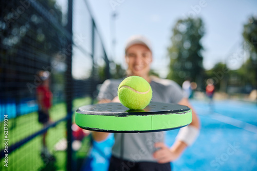 Close up of paddle tennis racket and ball with player in background. © Drazen