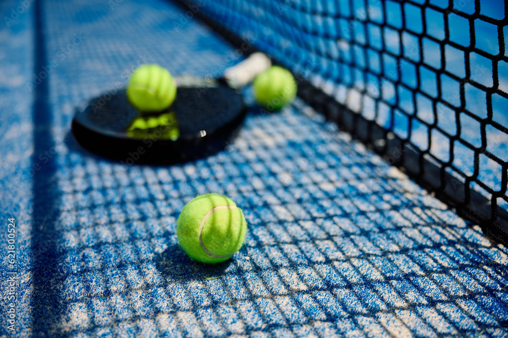 Yellow balls and racket on paddle tennis court.