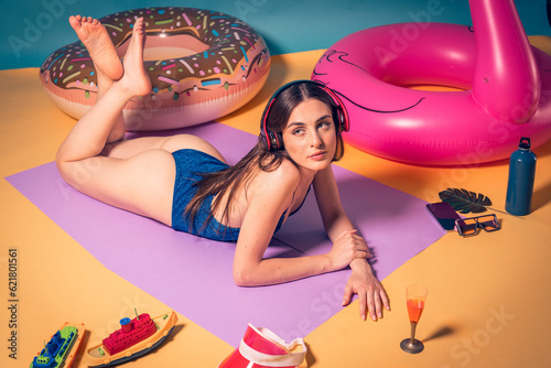 Funny summer photo shoot of beautiful brown hair model posing in studio wearing blue swimsuit and red hearphones barefoot. Studio light simulating sun in a photographyc studio of a charming woman photo