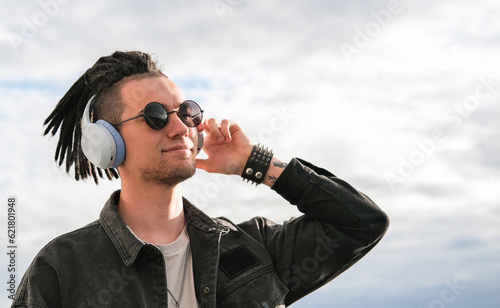 Portrait of a young guy with dreadlocks and piercings listening to music on headphones and enjoying moment