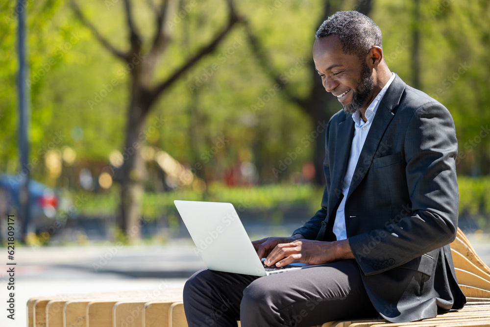 African american businessman working on laptop in the park and looking contented