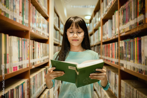 Little girl posing in public library room selecting for reading. girl chooses books on shelves learning from books and notebook is school education benefits of everyday reading concept.