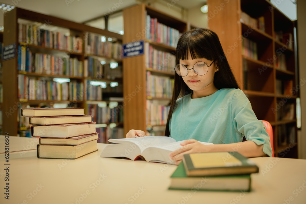 Little girl posing in public library room selecting for reading. girl chooses books on shelves learning from books and notebook is school education benefits of everyday reading concept. Little girl posing in public library room selecting for reading. girl chooses books on shelves learning from books and notebook is school education benefits of everyday reading concept.