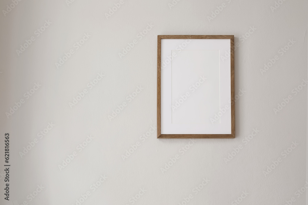 Vertical wooden picture frame mockup hanging on beige wall. Poster mock-upframe on pastel background in sunlight. Home interior with soft shadow, empty copyspace. Art display concept. Minimal interior
