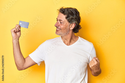 Man holding a credit card, yellow studio backdrop raising fist after a victory, winner concept.