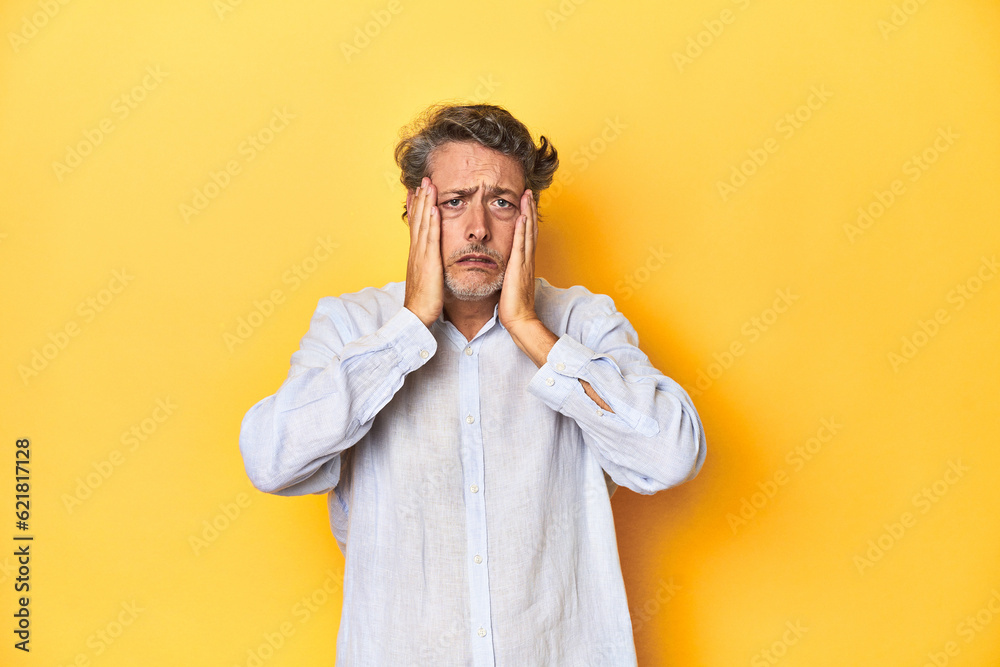 Middle-aged man posing on a yellow backdrop crying, unhappy with something, agony and confusion concept. Middle-aged man posing on a yellow backdrop crying, unhappy with something, agony and confusion concept.