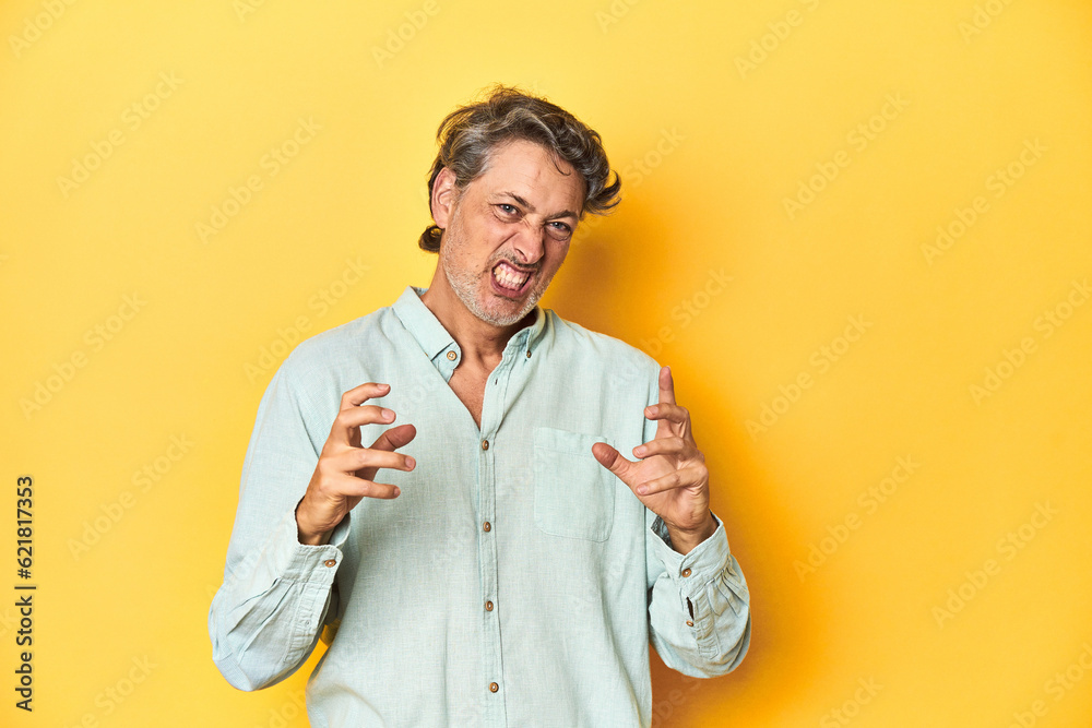 Middle-aged man posing on a yellow backdrop upset screaming with tense hands. Middle-aged man posing on a yellow backdrop upset screaming with tense hands.