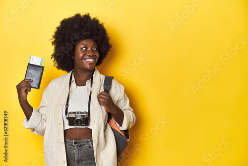 Travel-ready African-American woman holding an airplane ticket on a yellow background.