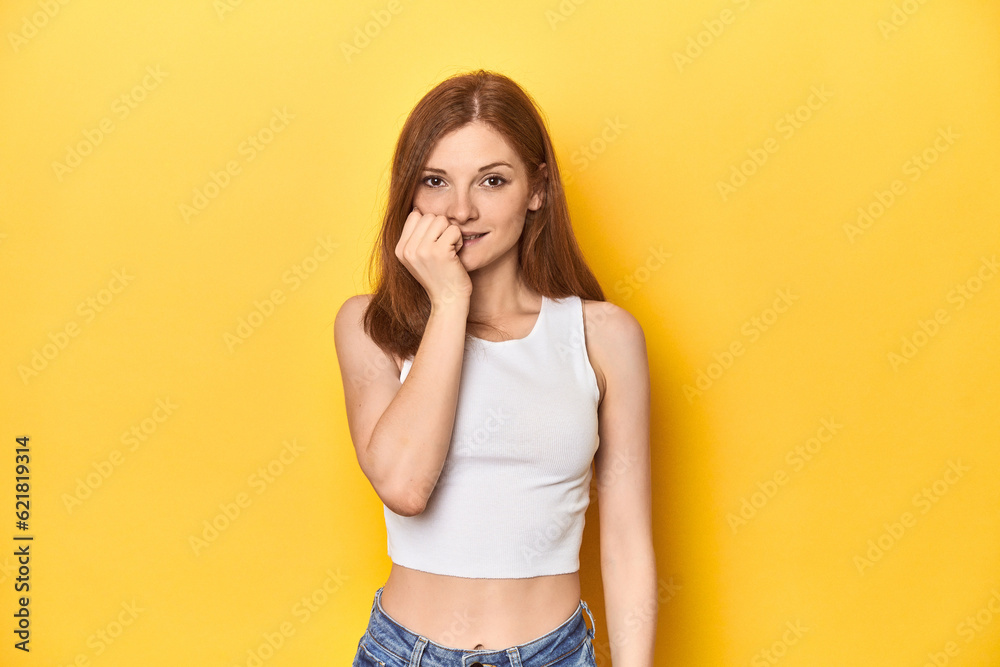 Redhead in white tank top, relaxed studio pose biting fingernails, nervous and very anxious. Redhead in white tank top, relaxed studio pose biting fingernails, nervous and very anxious.