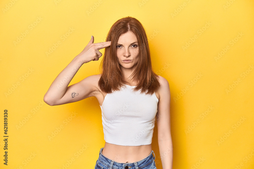 Redhead in white tank top, relaxed studio pose pointing temple with finger, thinking, focused on a task. Redhead in white tank top, relaxed studio pose pointing temple with finger, thinking, focused on a task.