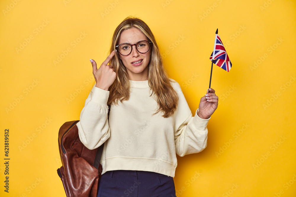 UK flag-waving student, Erasmus concept on yellow backdrop, showing a disappointment gesture with forefinger.