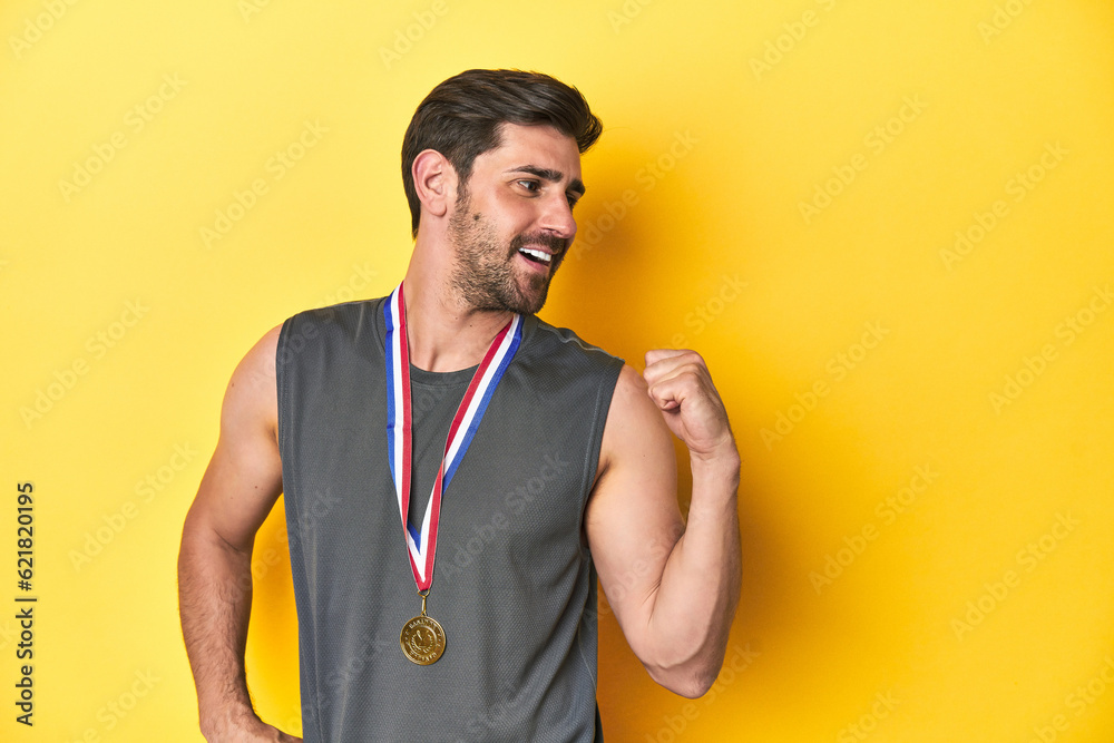 Athletic man with gold medal, yellow studio backdrop points with thumb finger away, laughing and carefree. Athletic man with gold medal, yellow studio backdrop points with thumb finger away, laughing and carefree.