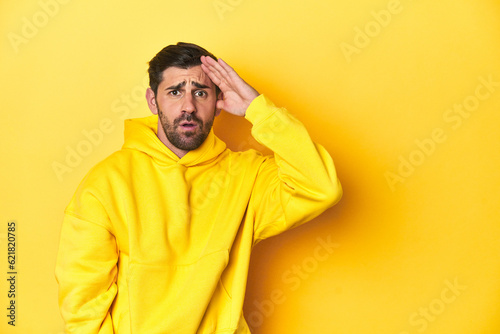 Man in yellow hoodie, monochrome studio backdrop shouts loud, keeps eyes opened and hands tense.