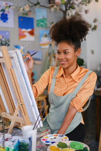 Portrait of cheerful student girl painting on canvas in art classroom. Art, creative learning and leisure activity concept