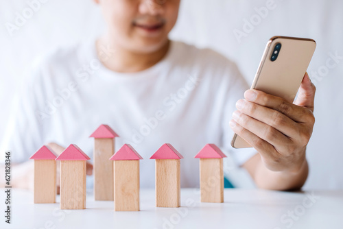 young man putting a triangle wooden block to show the construction of a wooden in the shape of a house, insurance business, real estate agent build a home concept.search data from smartphone