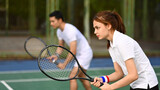 Determined female tennis player with racket standing in ready position to receive a serve. Outdoor sports and healthy lifestyle