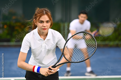 Determined female tennis player with racket standing in ready position to receive a serve. Outdoor sports and healthy lifestyle