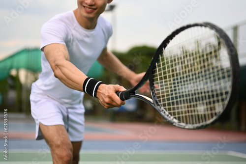 Smiling muscular man hitting ball with racket to return ball over net. Sport, fitness, training and active life concept © Prathankarnpap