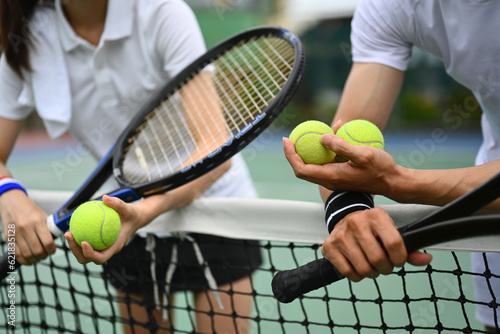 Experienced male tennis coach giving instructions to his student, standing by net at the outdoor tennis court