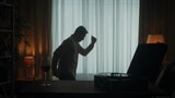 Vintage record player with a rotating vinyl record and a glass of red wine on the table close up. A carefree person dances merrily alone. The dark silhouette of a dancing man in the living room.