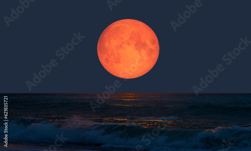 Night sky with orange moon in the clouds over the calm blue sea \