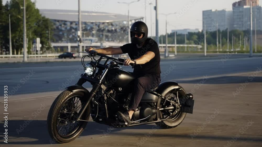 A stylish biker on a chrome motorcycle rides on asphalt in the summer. Black safety helmet. The man is wearing black clothes and sunglasses. Ride a bike in style. A stylish biker on a chrome motorcycle rides on asphalt in the summer. Black safety helmet. The man is wearing black clothes and sunglasses. Ride a bike in style.