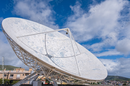 View of a large satellite dish to observe the cosmos  decorated with the lunar topography  with large white clouds in the background.