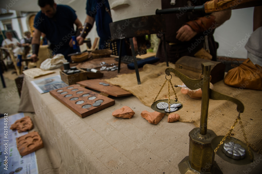 A glimpse of a Roman coin workshop at a lively recreation event, with craftsmen diligently creating ancient currency amidst the immersive historical atmosphere.
