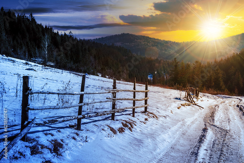 day and night time change concept. fence on snowy mountain slope near the forest in winter with sun and moon at twilight