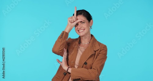 Business woman, loser sign and laughing in studio for mocking, winning or fun humour. Portrait of female model show emoji on forehead for competition, funny face or gesture on a blue background photo