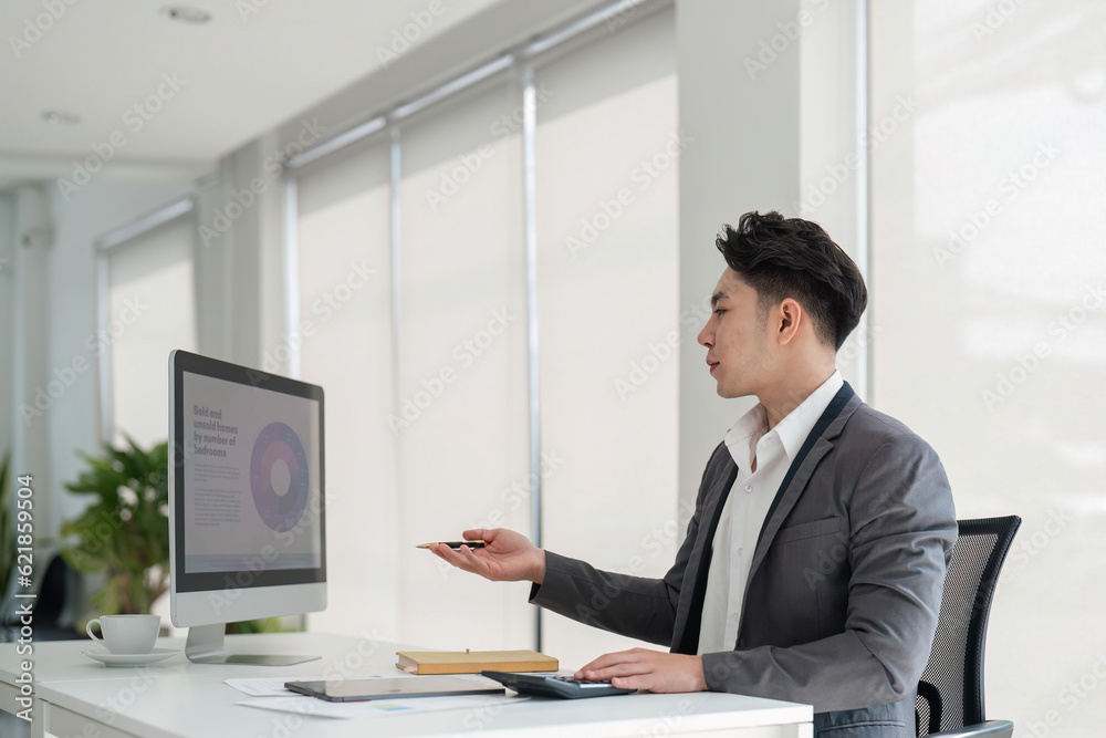 Handsome smiling businessman sitting in office and working on laptop screen Handsome smiling businessman sitting in office and working on laptop screen