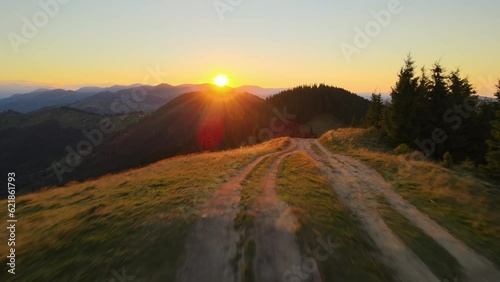 Offroad path crossing hill top. Dark dirt road illuminated with bright setting sun. Amazing sunset scenery in wild mountain forest. Beautiful nature landscape