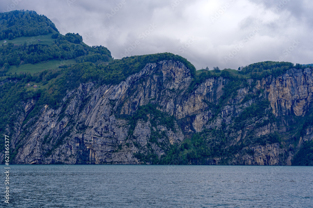 Obraz premium Scenic landscape with cliff and woodland at lakeshore of Lake Lucerne seen from passenger ship on Lake Lucerne on a cloudy spring day. Photo taken May 18t, 2023, Treib, Canton Uri, Switzerland.