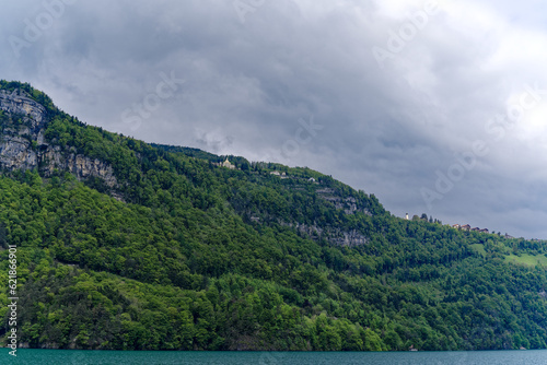 Fototapeta Naklejka Na Ścianę i Meble -  Scenic landscape with rock, cliff and woodland with mountain village Seelisberg at lakeshore of Lake Uri on a cloudy spring day. Photo taken May 18th, 2023, Seelisberg, Switzerland.