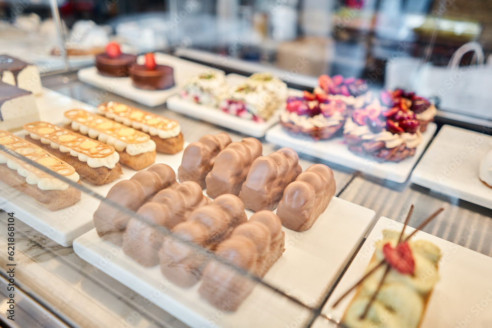 A variety of cakes covered with chocolate and decorated with pistachio mousse. A showcase in a pastry shop with delicious desserts with fresh berries and cream. Delicious pastries in the coffee shop.