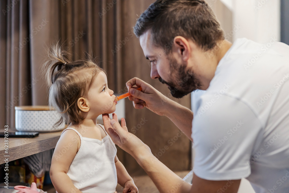 A father is giving a syrup and medicine to his baby girl. A father is giving a syrup and medicine to his baby girl.