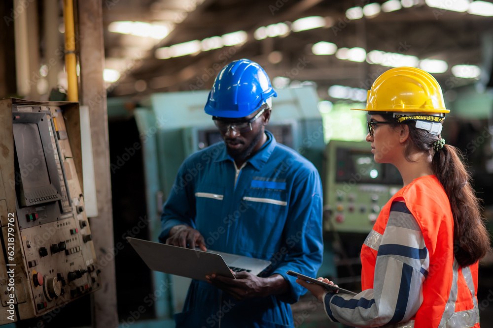 Caucasian woman programmer engineer and african man Technician operator machine is working in factory, checking lathe machinery operating with laptop to maintain safety of work, Safety first concept. Caucasian woman programmer engineer and african man Technician operator machine is working in factory, checking lathe machinery operating with laptop to maintain safety of work, Safety first concept.