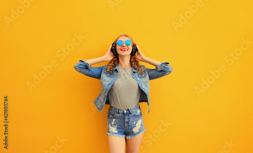 Portrait of happy smiling young woman in wireless headphones listening to music on yellow background