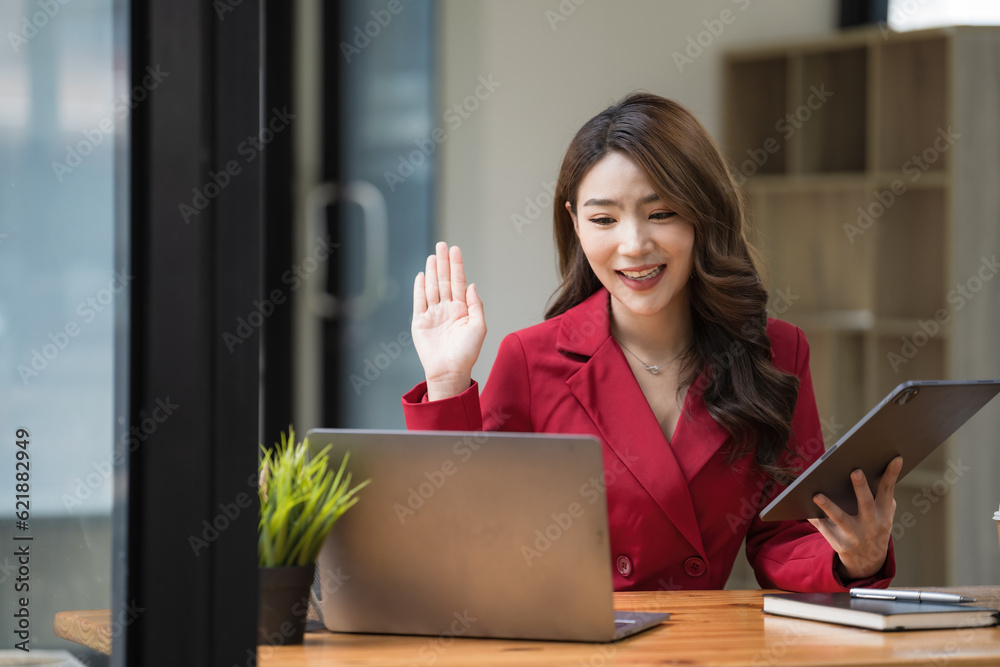 A beautiful Asian businesswoman sitting in her private office is talking to her partner via video call on her laptop, she is a female executive of a startup company. Concept of financial management. A beautiful Asian businesswoman sitting in her private office is talking to her partner via video call on her laptop, she is a female executive of a startup company. Concept of financial management.
