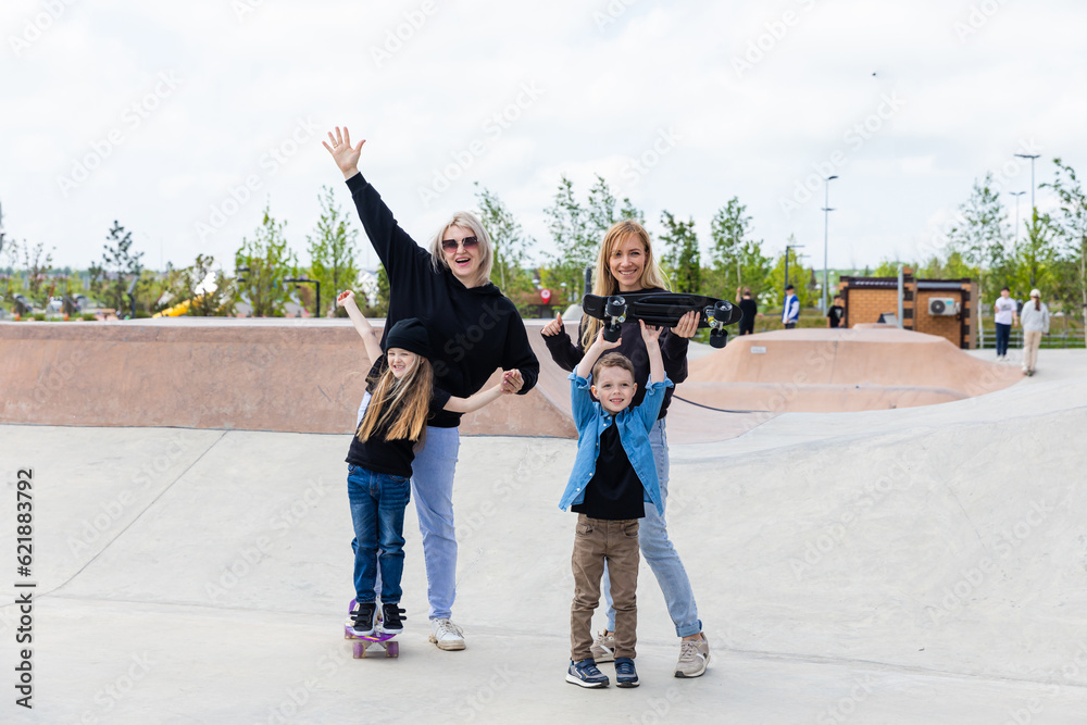 Obraz premium Two moms with two kids boy and girl having fun in a skatepark. cheerful group of friends spending time together