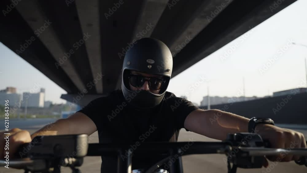 A stylish biker looks at the camera and pumps the throttle stick in a motorcycle. Black safety helmet. Sunglasses. Brutal black color in the motorcycle and clothes of a middle-aged man. A stylish biker looks at the camera and pumps the throttle stick in a motorcycle. Black safety helmet. Sunglasses. Brutal black color in the motorcycle and clothes of a middle-aged man.