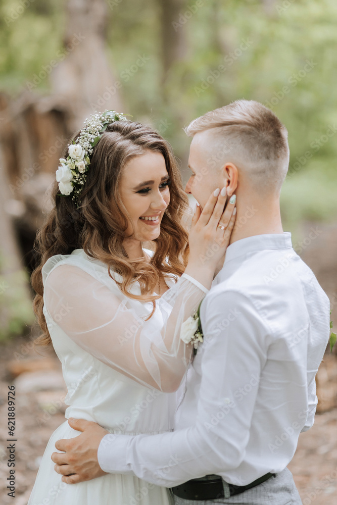 Wedding walk in the forest. The bride and groom look at each other. Portrait of a couple in love in the forest, the bride looks at him and smiles sincerely Wedding walk in the forest. The bride and groom look at each other. Portrait of a couple in love in the forest, the bride looks at him and smiles sincerely