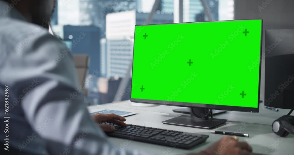 Over the Shoulder Footage of a Close Up Computer Screen with Green Mock Up Template. Anonymous Man Working in Office, Browsing Internet and Researching Business ata Online
