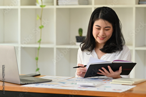 Business data analysis concept with asian businesswoman working at desk with full of graphs, diagrams and figures of financial documents on table.